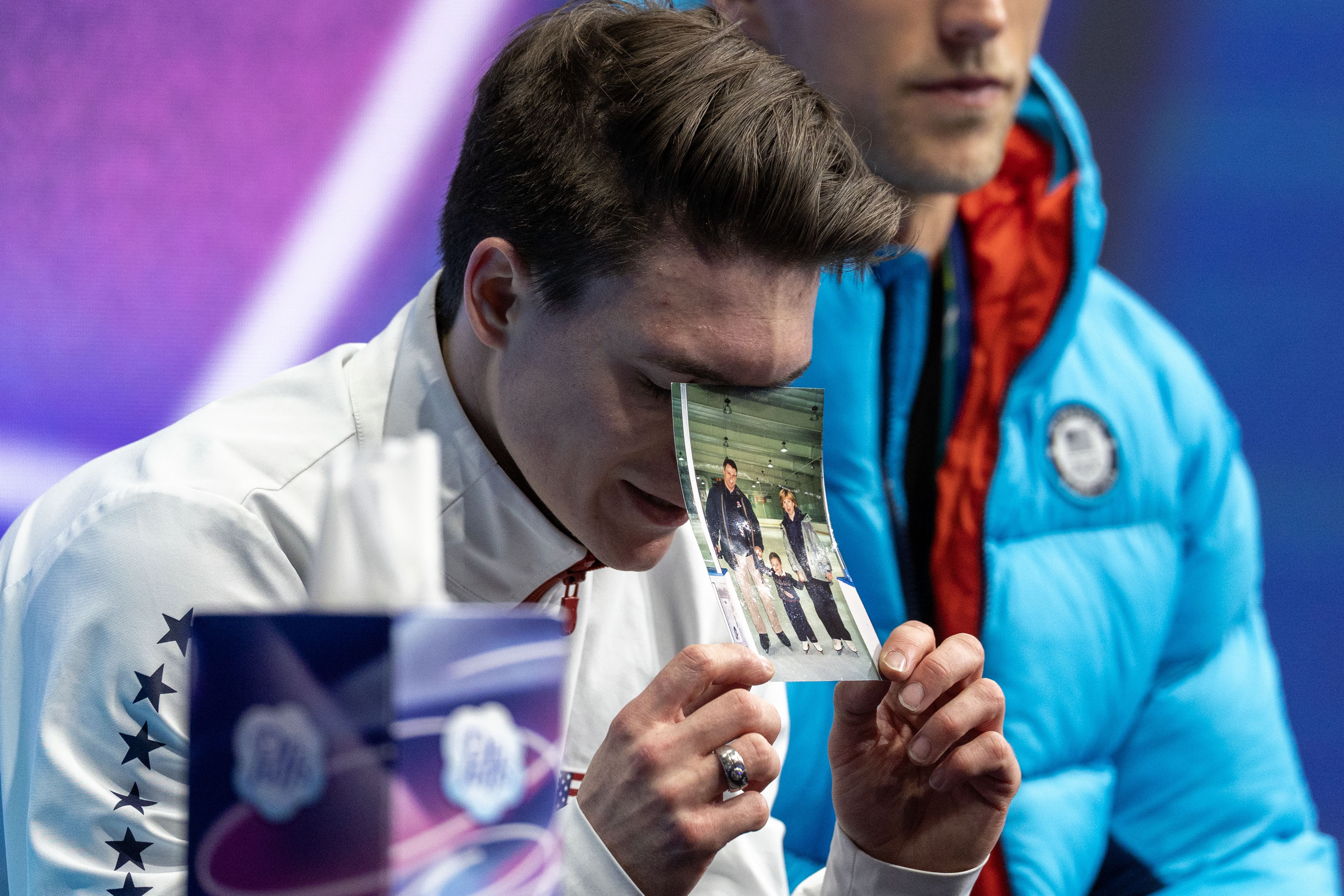 MILAN, ITALY - February 13: Maxim Naumov of the United States with a picture of his parents as he awaits his score after performing his routine during the Figure Skating, Men's Singles Skating-Free Skating competition at the Milano Ice Skating Arena at the Milano Cortina Winter Olympic Games 2026 on February 13th, 2026 in Milan, Italy.  (Photo by Tim Clayton/Getty Images)