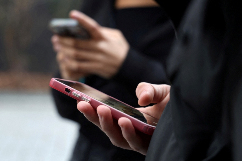 FILE PHOTO: Teenagers look at their mobile phone screens during an interview with Reuters about the bill aimed at banning the use of social networks for those under 15 and mobile phones in high schools from the start of the 2026 school year, in Paris, France, February 20, 2026. REUTERS/Manuel Ausloos/File Photo