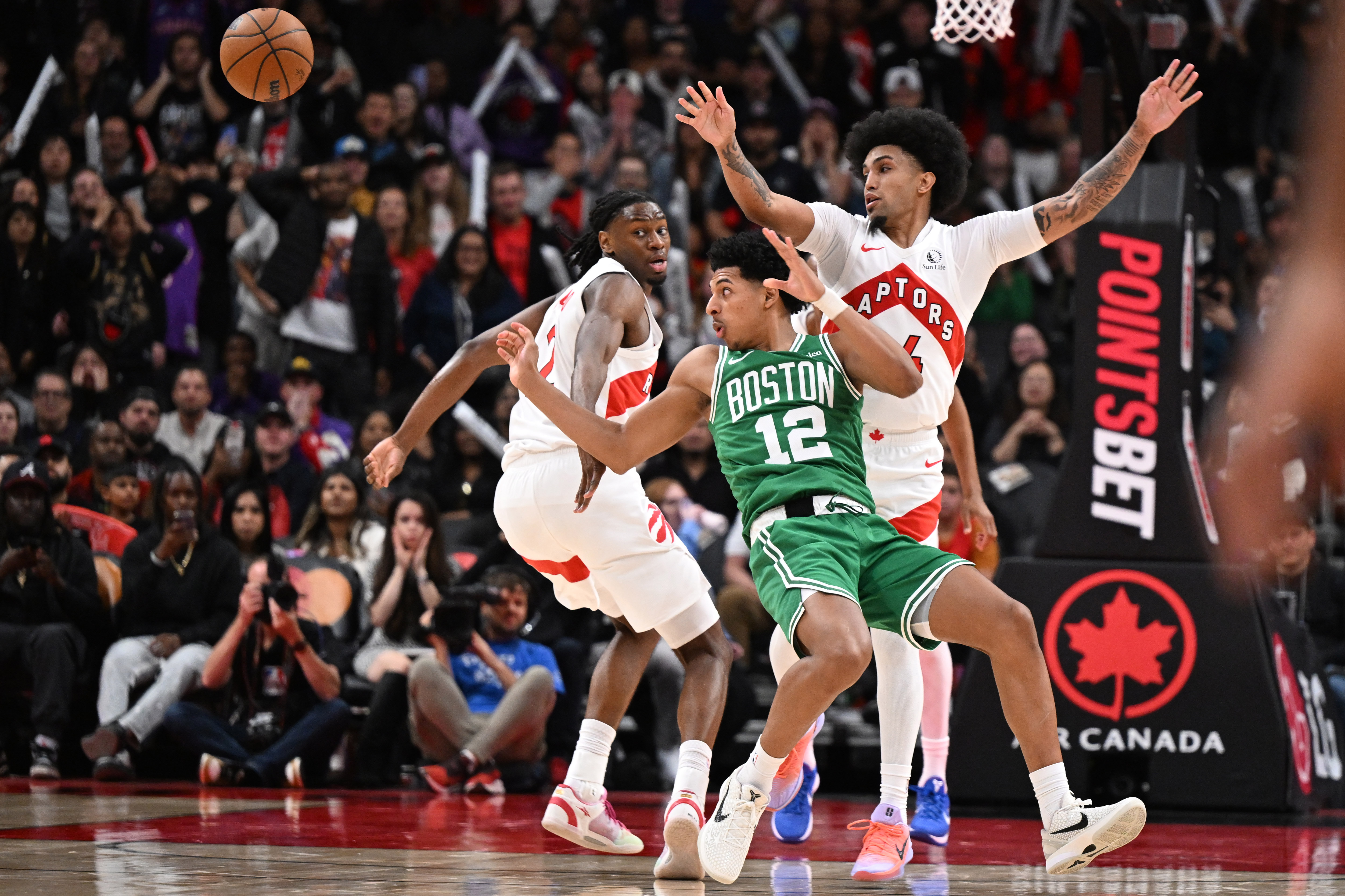 Oct 10, 2025; Toronto, Ontario, CAN;  Boston Celtics forward R.J. Luis Jr. (12) loses control of the ball against Toronto Raptors guard Chucky Hepburn (24) and forward Jonathan Mogbo (2) in the second half at Scotiabank Arena. Mandatory Credit: Dan Hamilton-Imagn Images