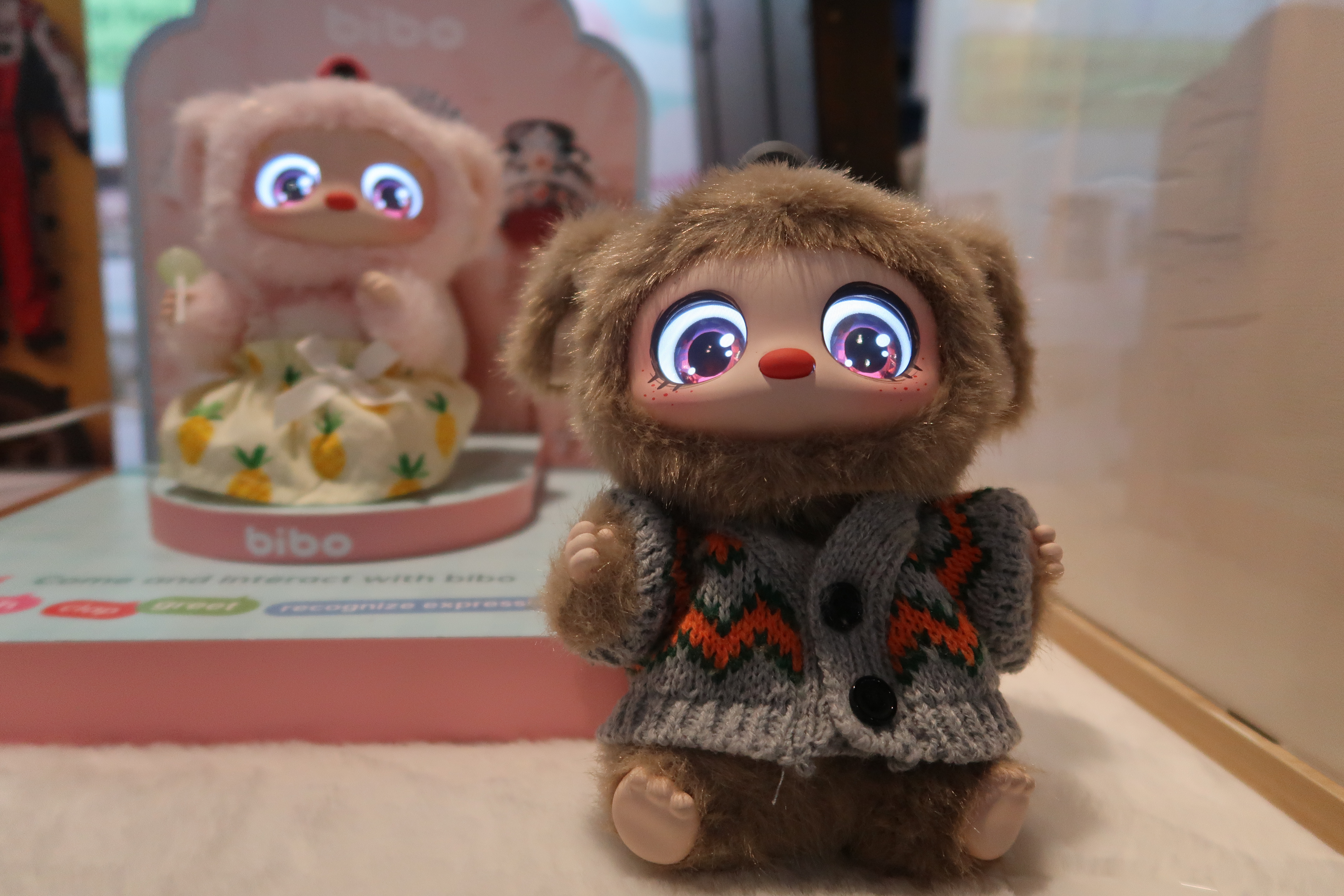 A Labubu-like AI toy with brown fur and big eyes and wearing a gray sweater 