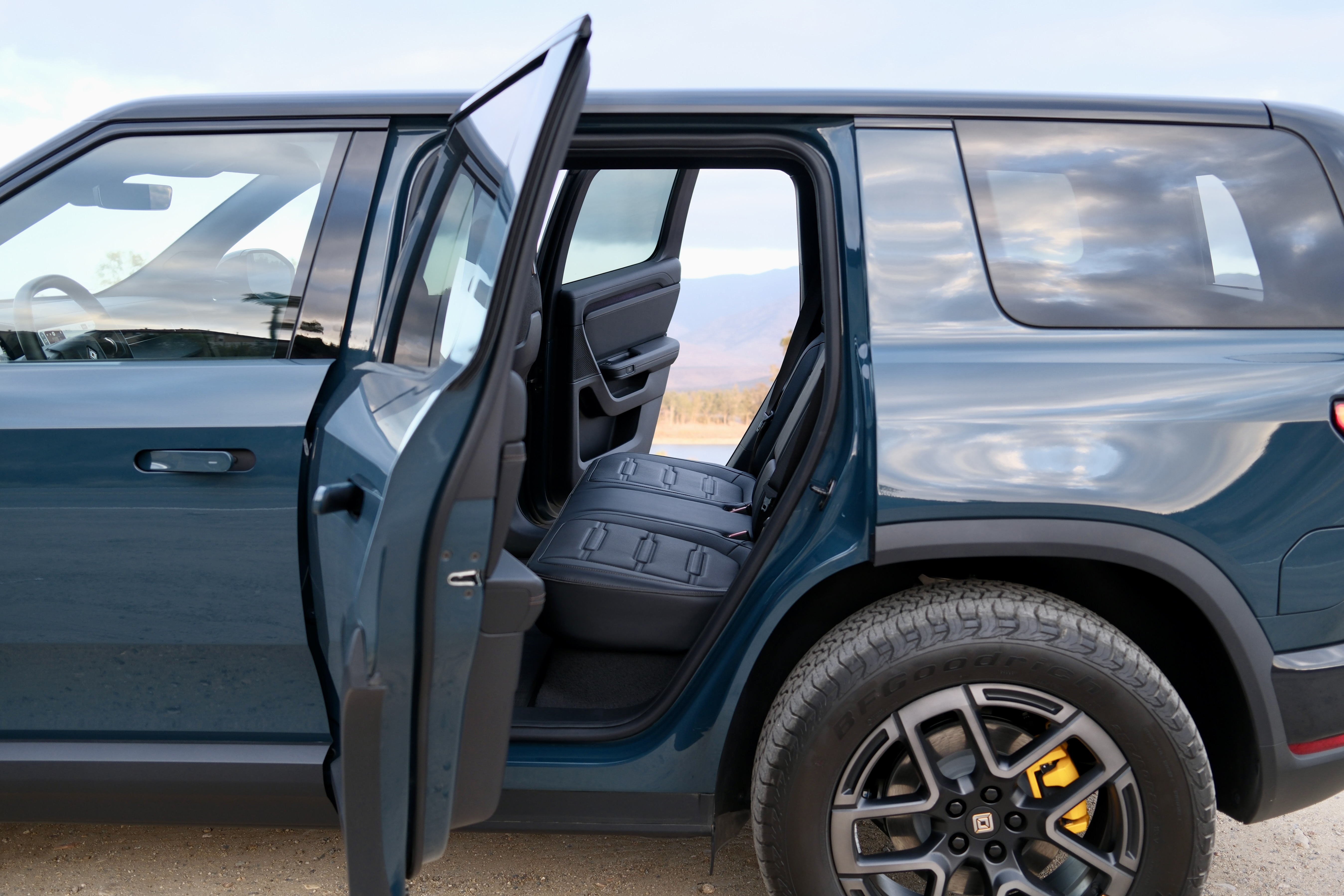 Both rear doors of the Rivian R2 open, looking through to a lake