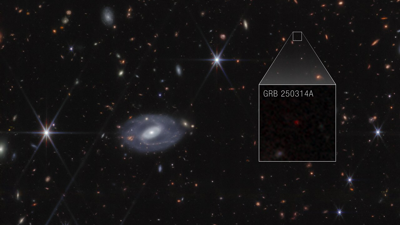 Webb image shows hundreds of galaxies of all shapes and sizes against the black background of space. Toward the center-left is a large white spiral galaxy that is almost face-on. To the right of this is a large box, which zooms in on an area at top right. Within the box is a faint red dot at the center, with the label GRB 250314A.